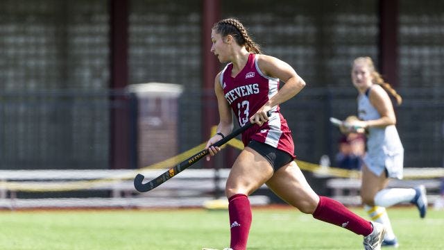 Field hockey player runs up the field with the ball
