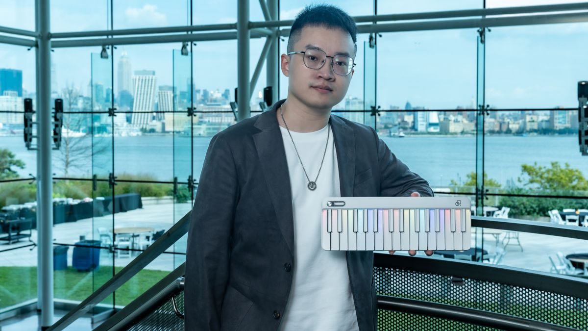 Bohan Zhang stands holding his PopuPiano device with the New York City skyline in the background.