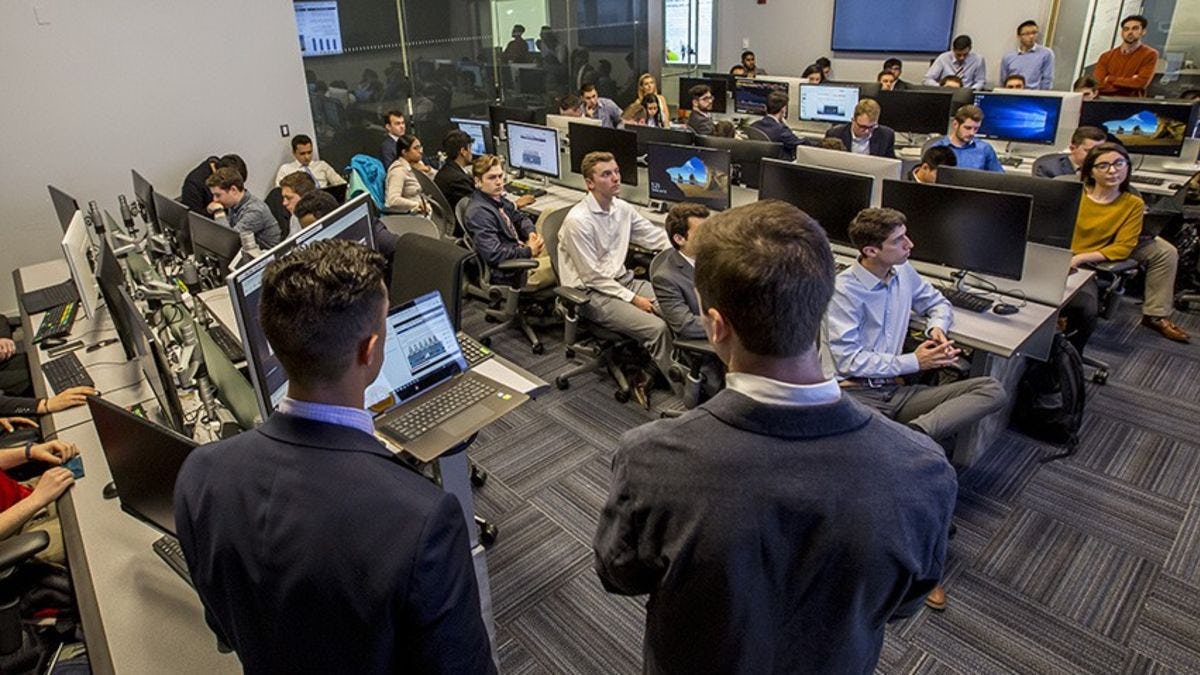A class in a Bloomberg finance lab being led by two male students wearing dark suits.