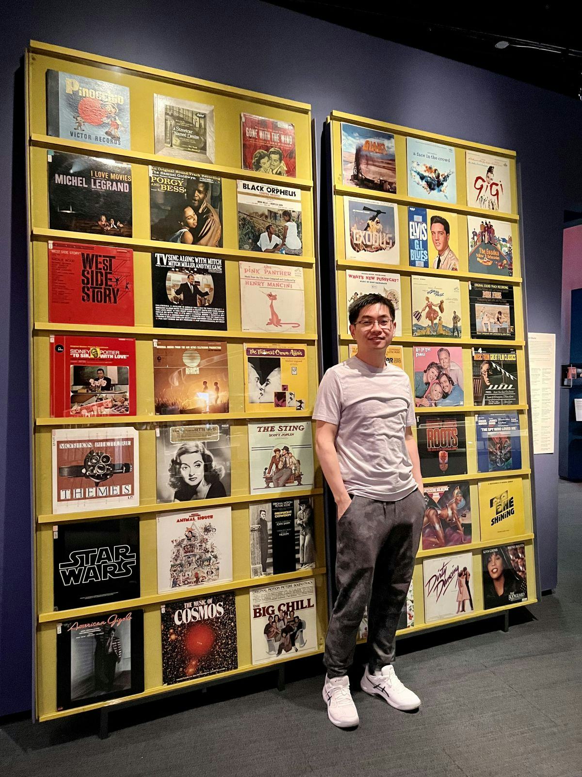 Shucheng Yu standing in front of a wall covered in Broadway and music posters