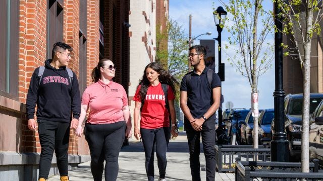 Four students walk on campus sidewalk in Stevens gear
