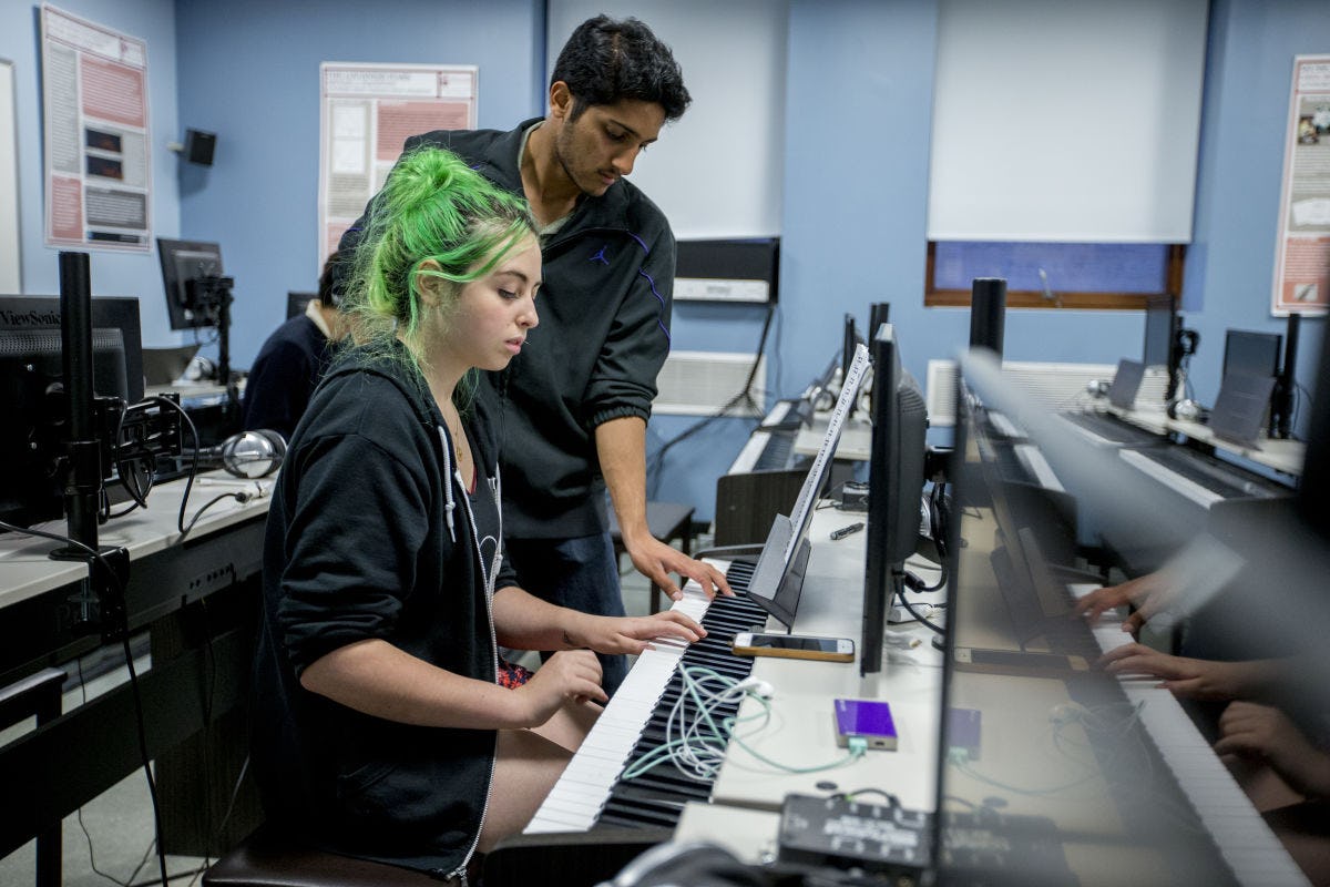 Two students work on a musical keyboard and computer set up.