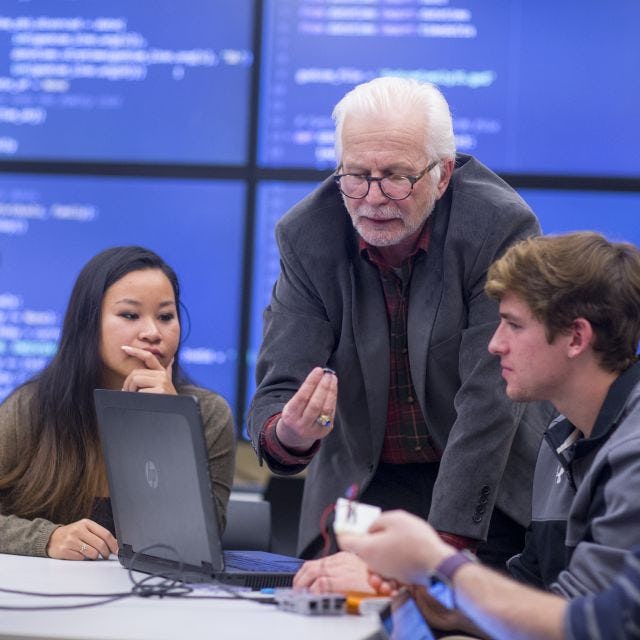 Students surrounding a laptop and working with a professor 