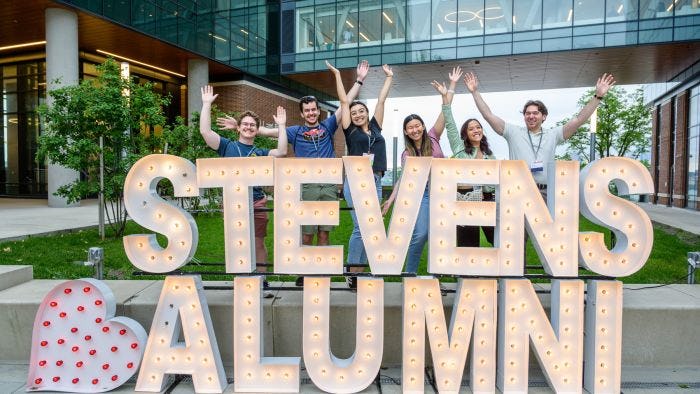 Alumni pose in front of a Stevens Alumni sign