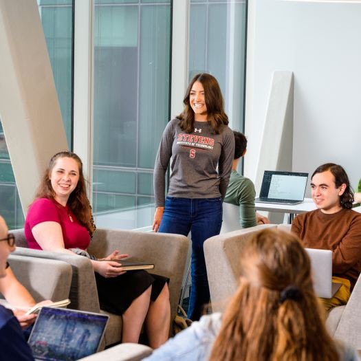 A group of students chatting in the UCC skybridge while other students study in the background.