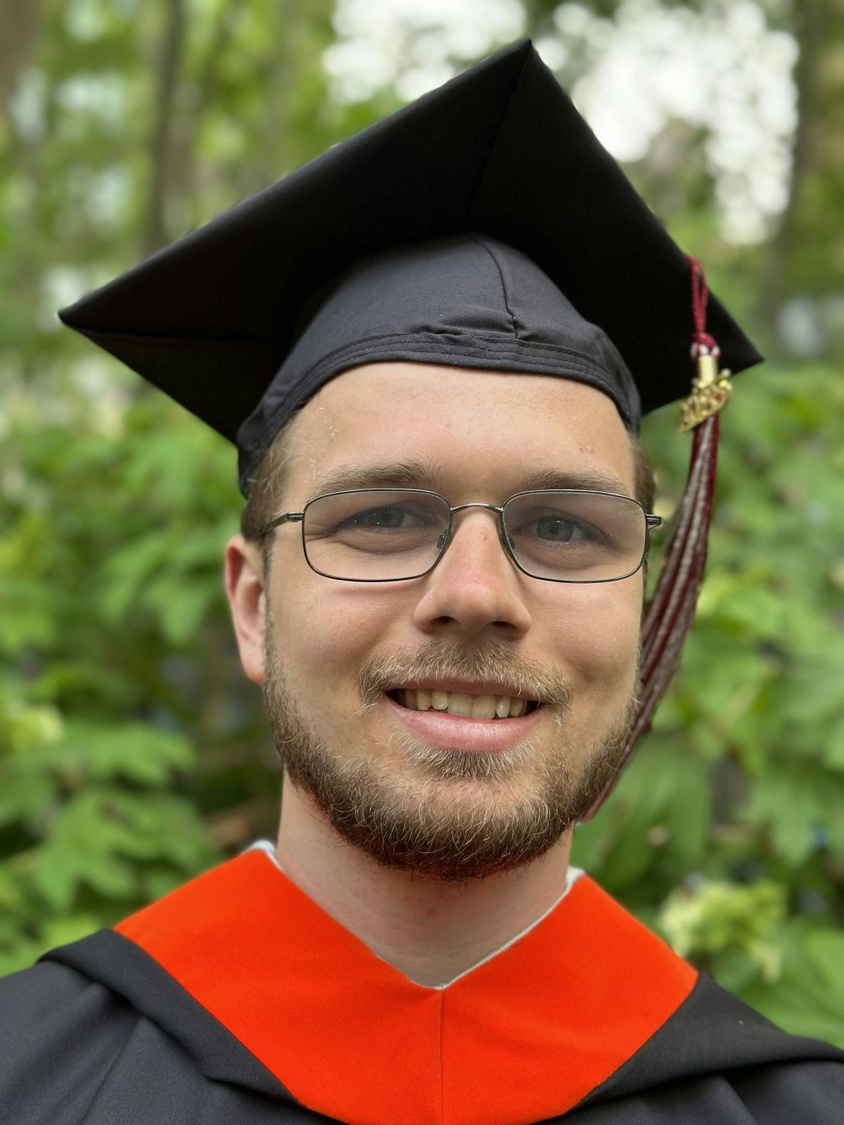 Erik Cederstav ’23 smiles outside while wearing mortarboard and graduation robe