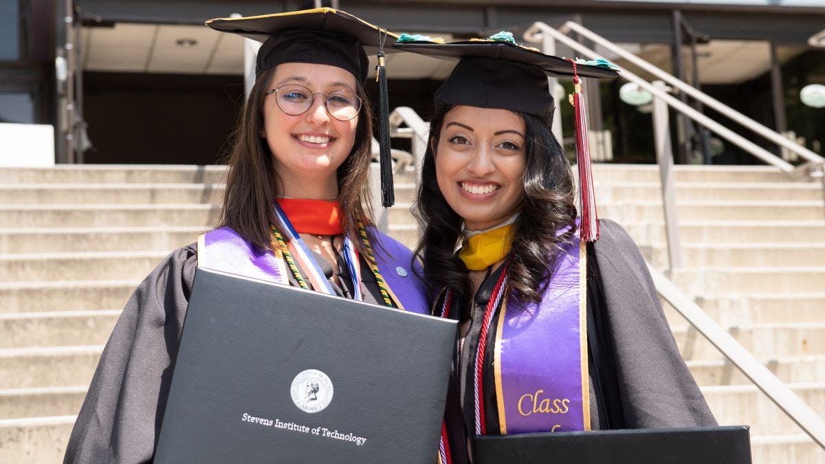Two women graduates dressed in regalia showing off their degrees