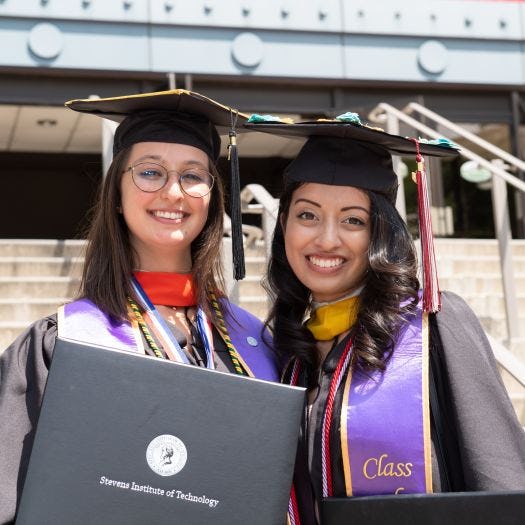 Two women graduates dressed in regalia showing off their degrees