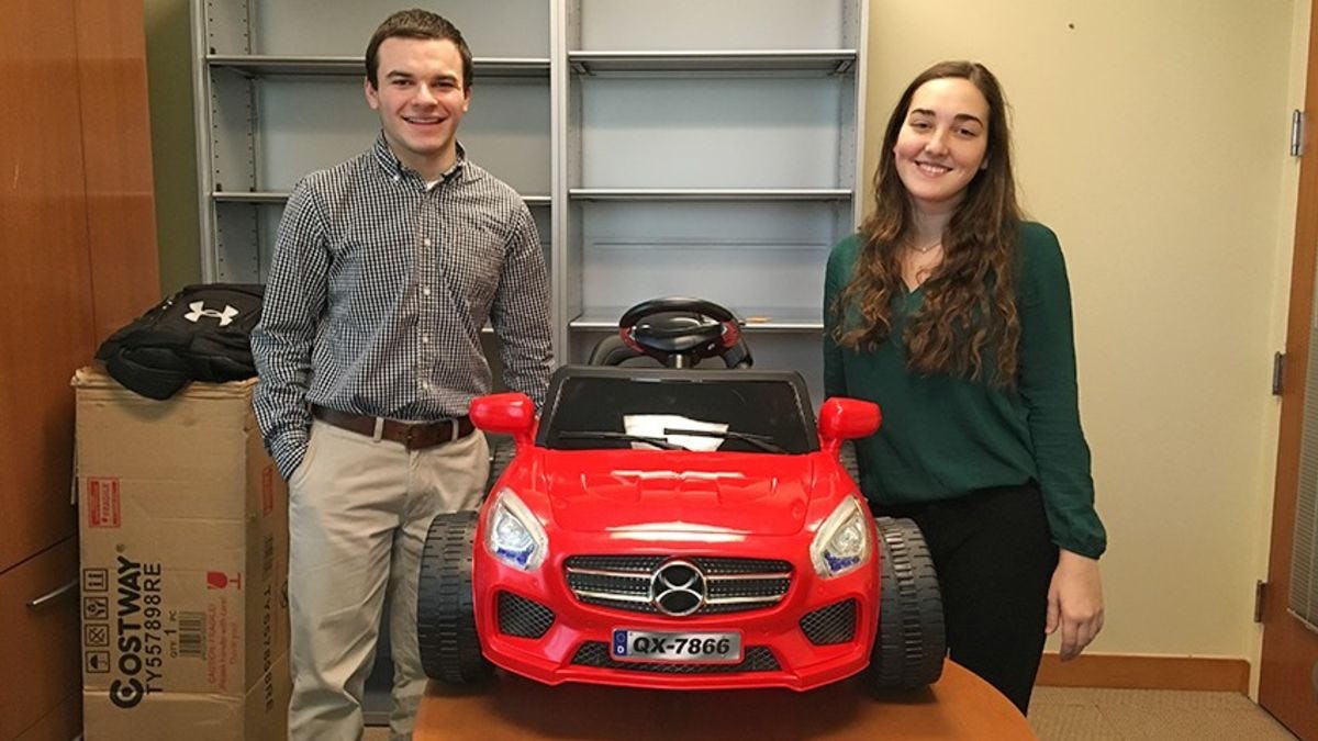 A male and female student in a Stevens office, standing with a red toy car they rewired for students with disabilities.