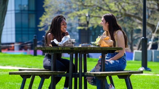 Two female students laugh outside on picnic table