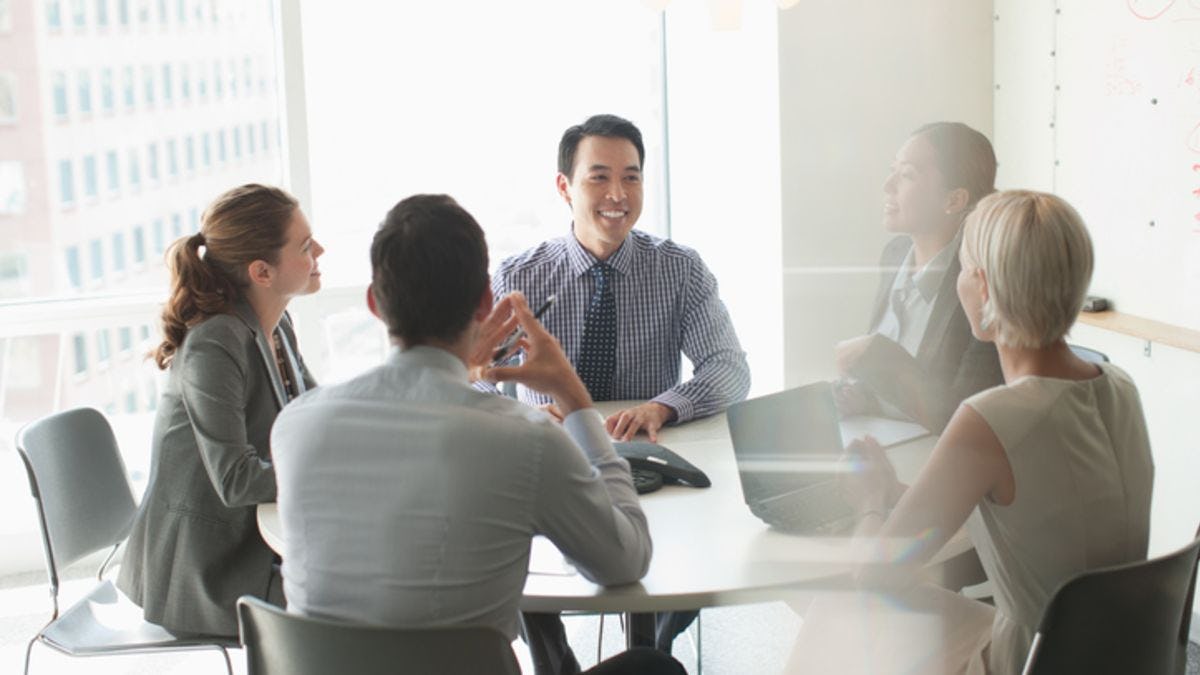 one man smiling with group of coworkers around a conference table