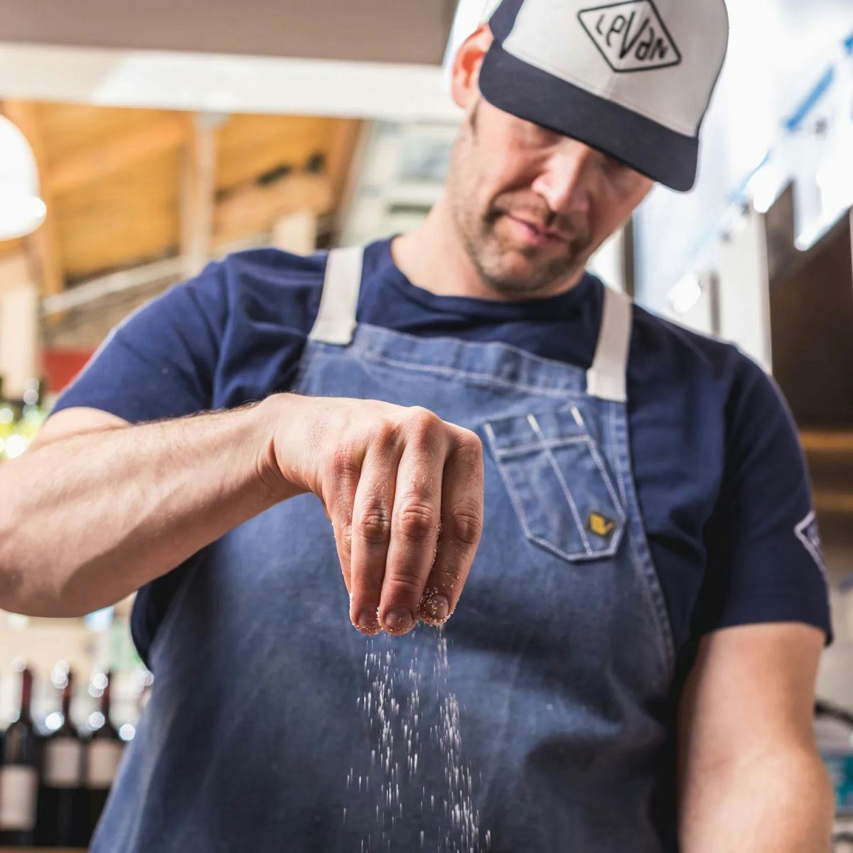 Chef sprinkling salt and wearing a hat that says "Leven"
