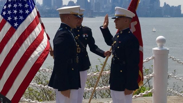 Two servicemen saluting with flags on waterfront