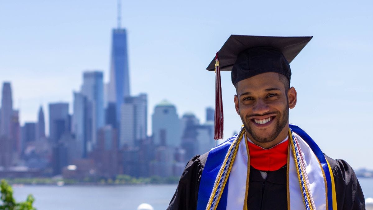 Jose Angeles-Ovalles, wearing his cap and gown, standing on Castle Point with Manhattan in the background on Commencement Day