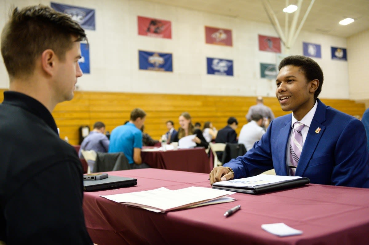 A male company representative (left) interviews a male co-op student at one of the tables inside Canavan Arena