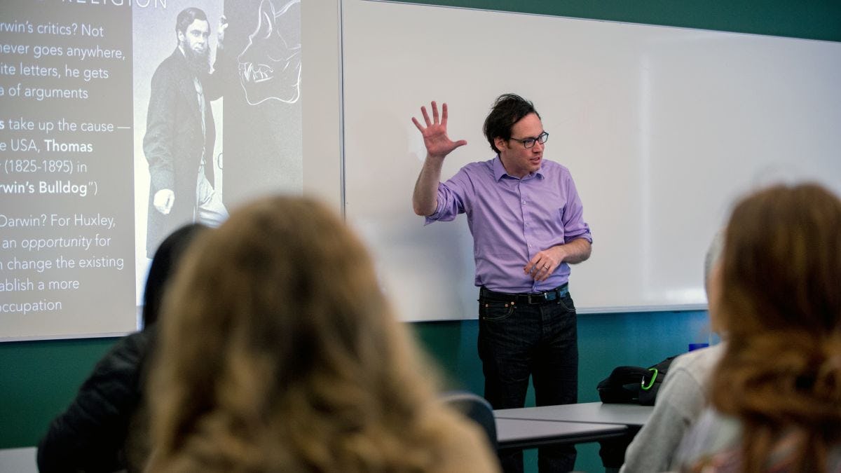 Professor gestures to class in front of presentation