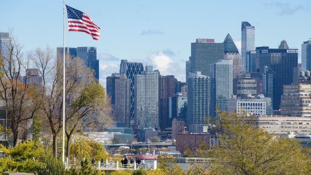 American flag flys on Stevens campus at Castle Point with New York city in background.