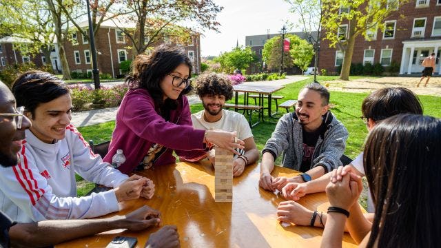 Students gather outside to play Jenga on a table on campus