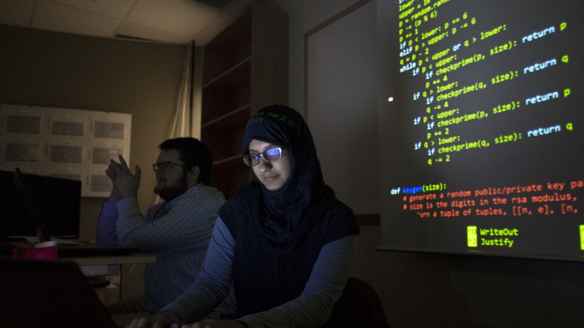 Woman student in classroom with computer code on screen behind her