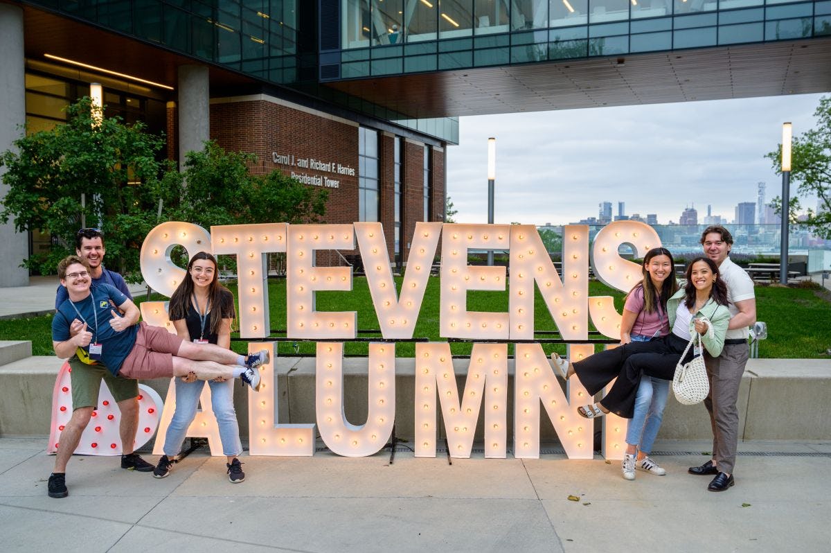 Alumni pose on campus in front of the Stevens Alumni illuminated sign during Alumni Weekend 2023