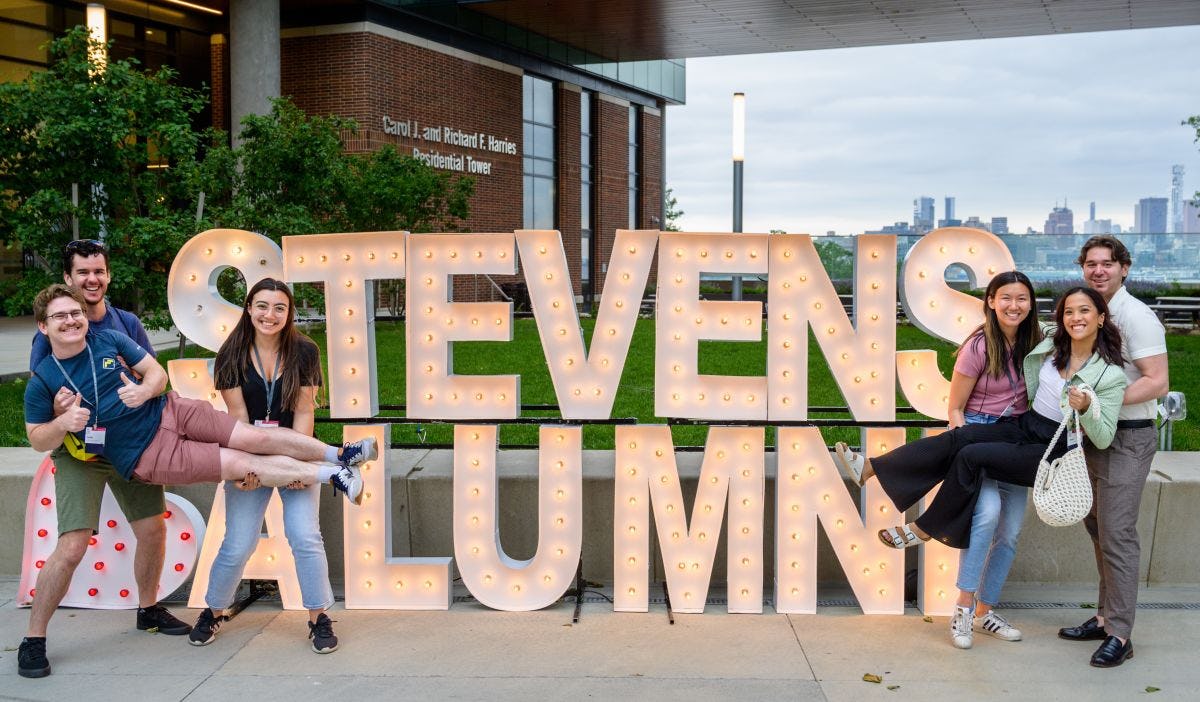 Alumni pose on campus in front of the Stevens Alumni illuminated sign during Alumni Weekend 2023