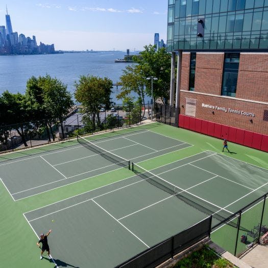 Students play on the Battista Family Tennis Courts with New York City skyline in the background