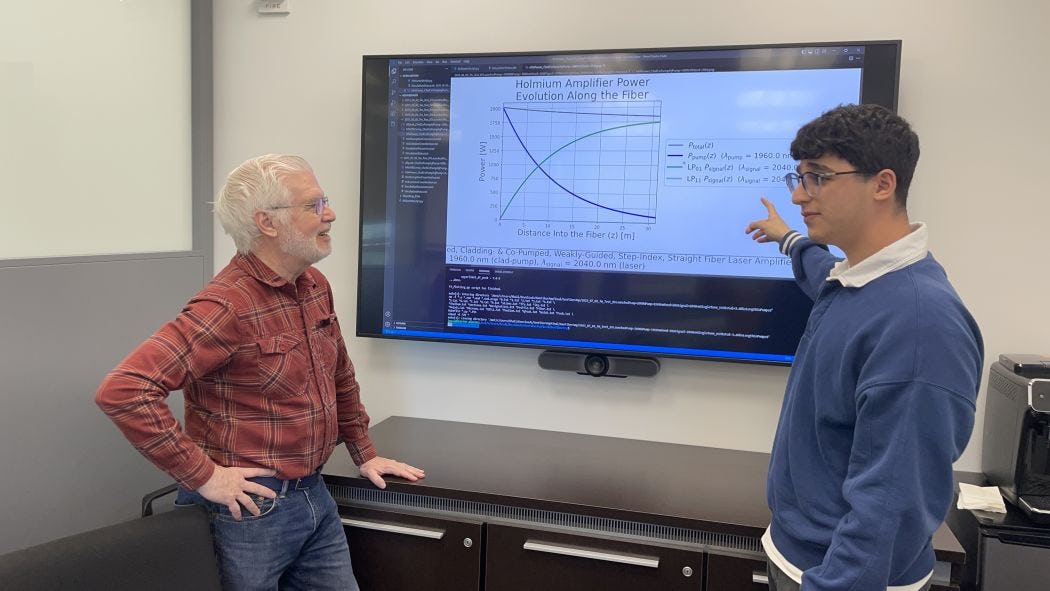 A photo of Ed Whittaker and Khalid Musa talking in front of a big screen with physics equations