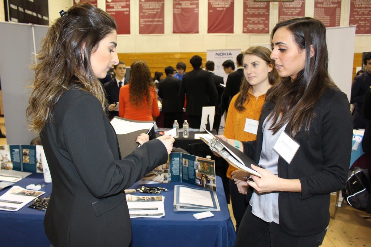 A female student on the left looks down at a business card while two female recruiters, on the right, look on