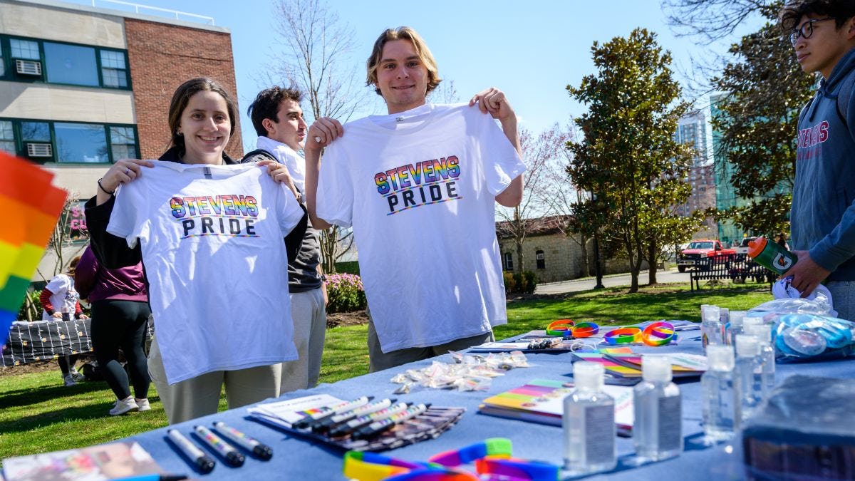 Photo of students holding up Stevens Pride t-shirts at a Pride themed table