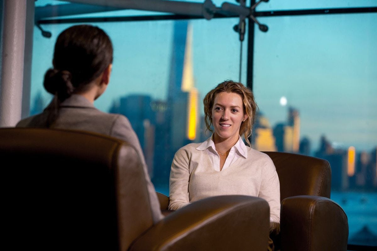 Two women talking while sitting in chairs with NYC skyline in background