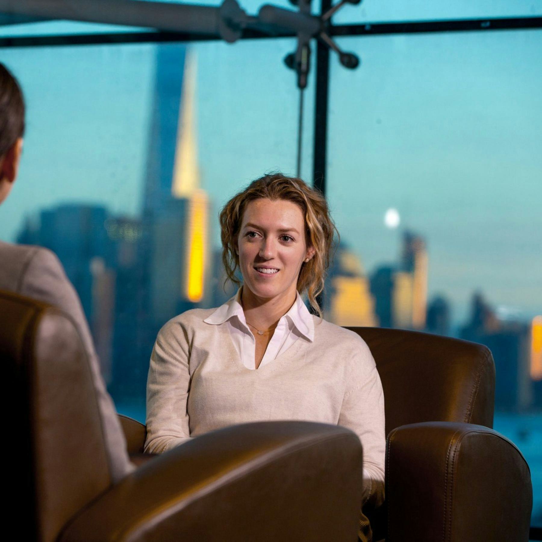 Two women talking while sitting in chairs with NYC skyline in background