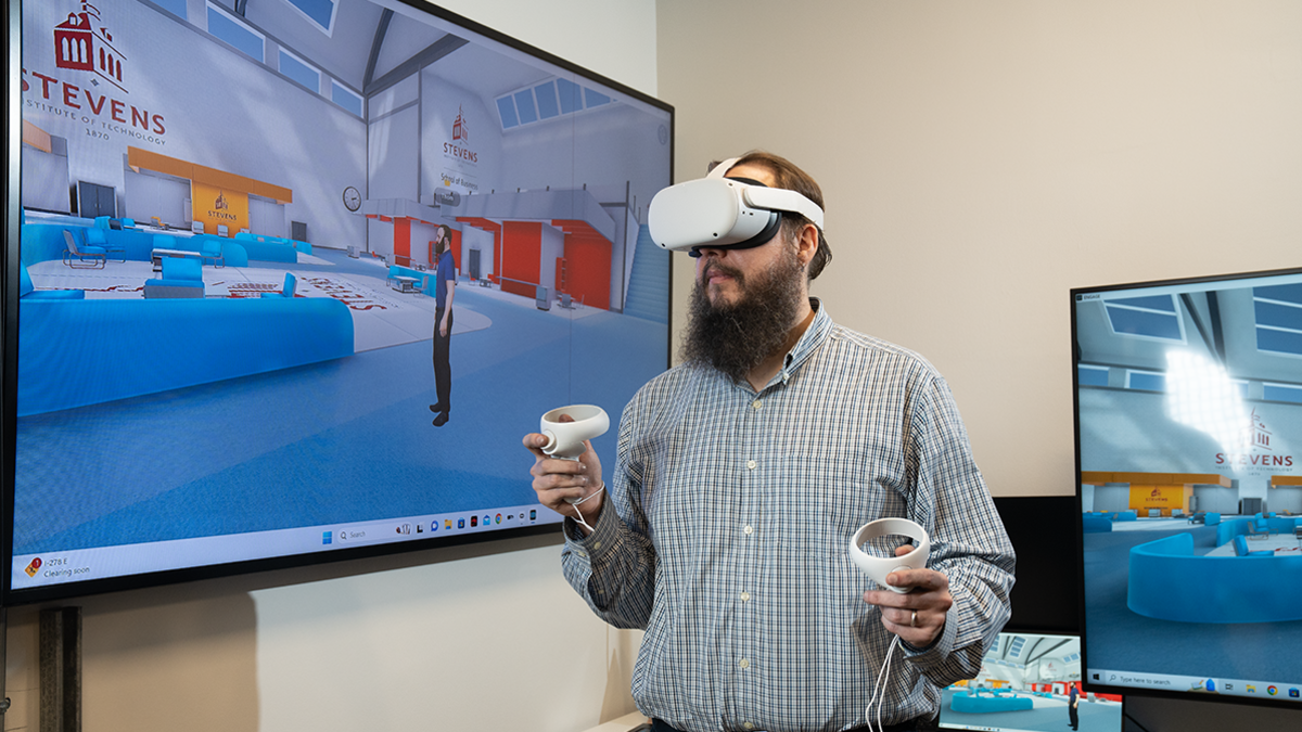 Professor Thomas Lonon wears a virtual reality headset in front of a television screen projecting what it looks like inside the headset.