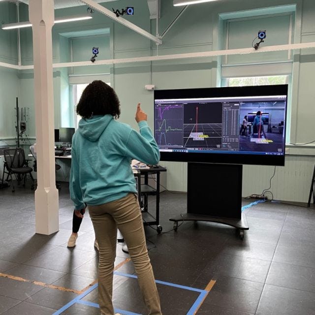 A high school girl stands in front of a computer screen watching her movements mirrored via sensors