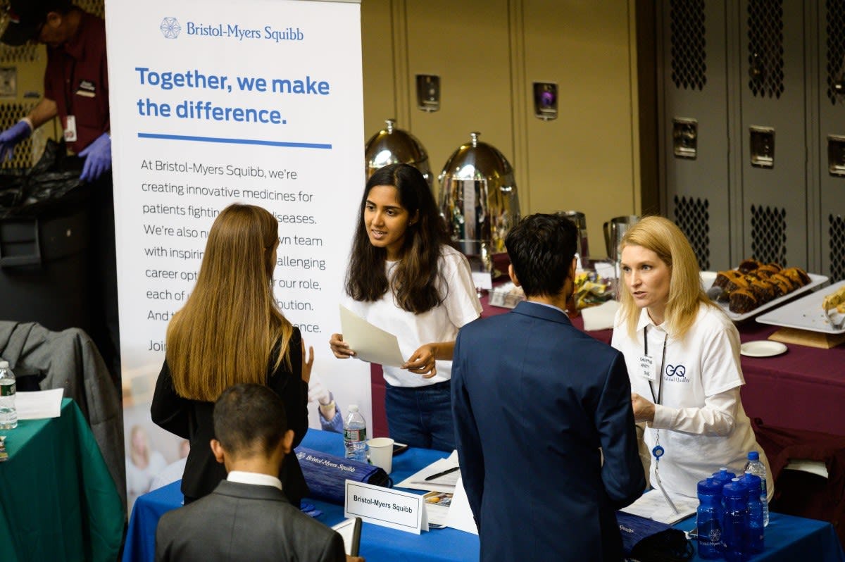 Two Stevens students speak to two recruiters at the Bristol-Myers Squibb table