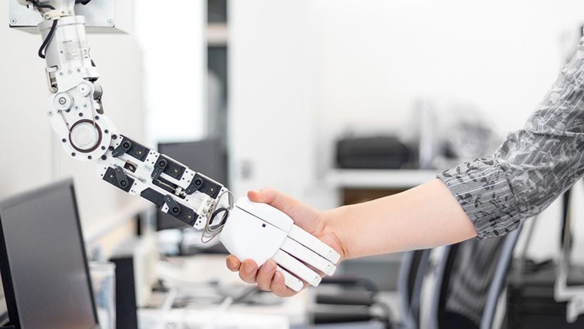 A female shakes hands with a robot in a busy laboratory.