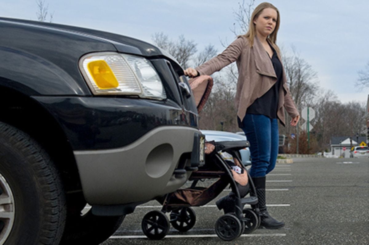 A woman walks alongside her stroller from behind a parked SUV.