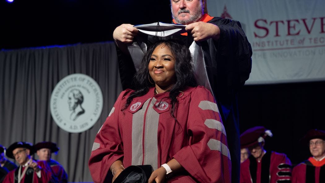A Ph.D. graduate is hooded by her advisor at commencement.