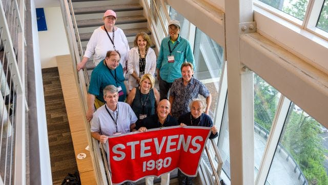 Alumni pose on stairs holder a Stevens Class of 1980 banner