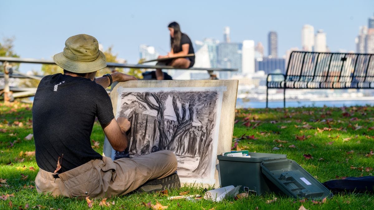 Student draws trees and buildings in charcoal with NY skyline in background