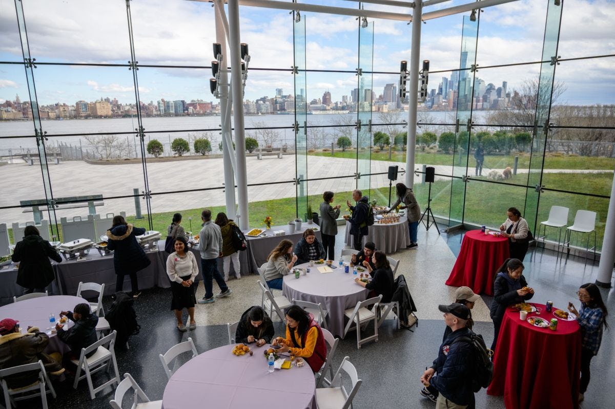 Shot from up high looking down at people mingling in a large room, with a sweeping window overlooking Manhattan in the background -- in the Babbio building