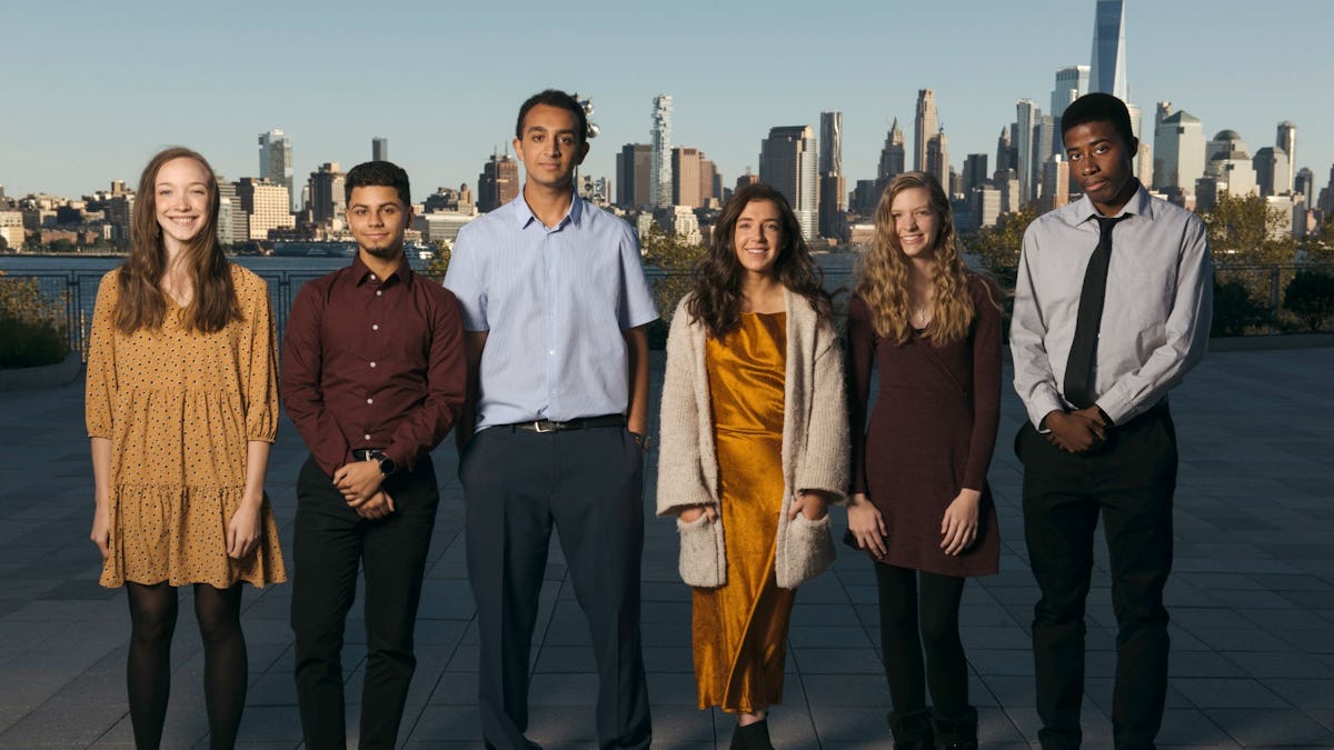 Group of six students pose in front of New York skyline.