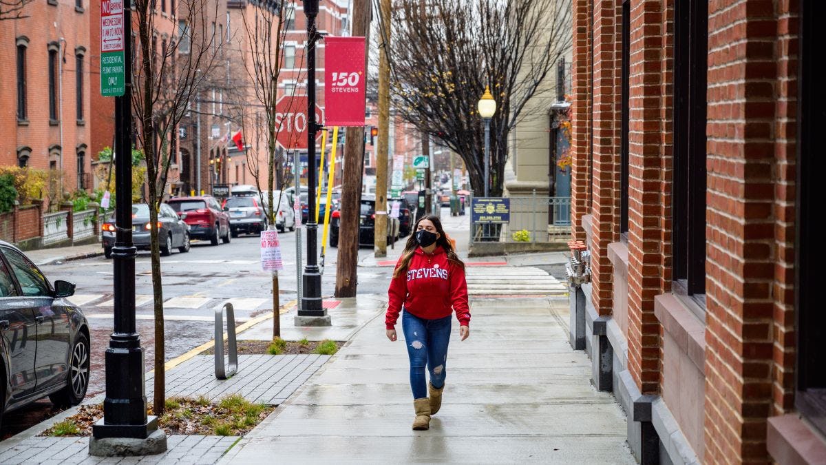 Female Stevens student in red hoodie walking on a Hoboken sidewalk after a rainshower.