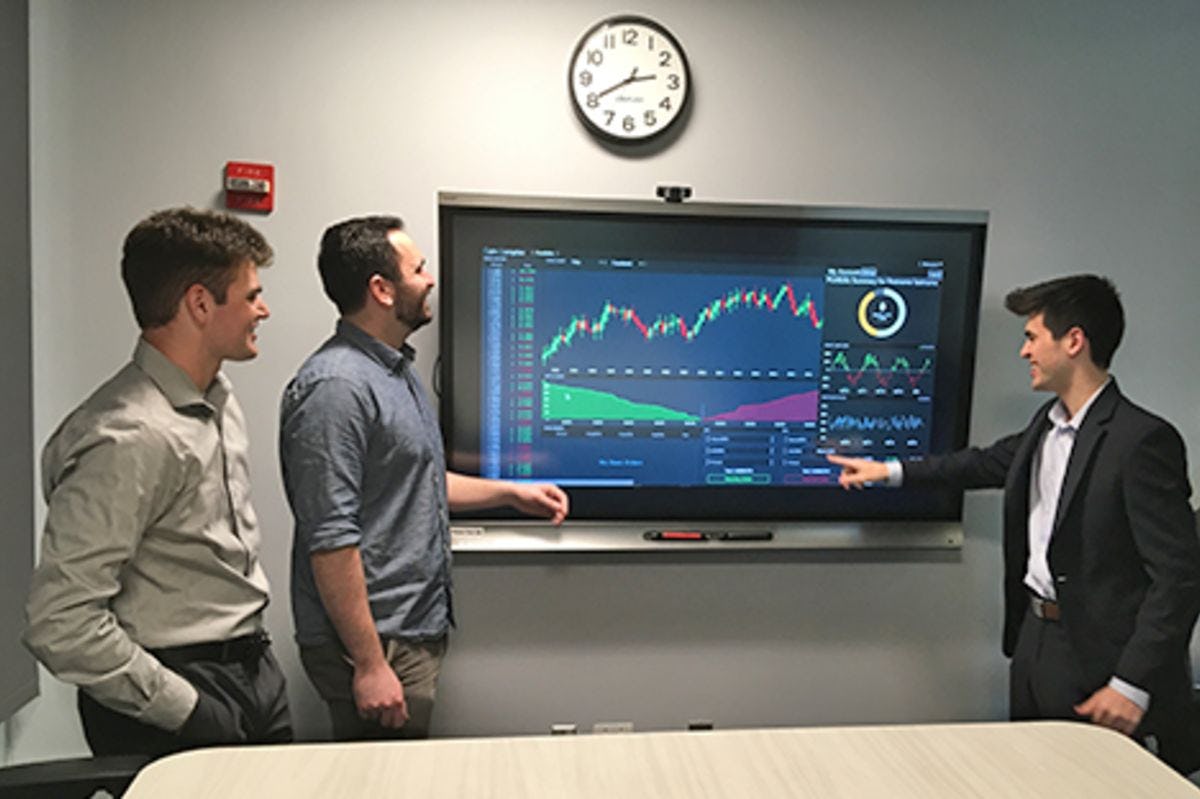 The three business students on Coin Complex walk through the exchange's interface in a high-tech lab.