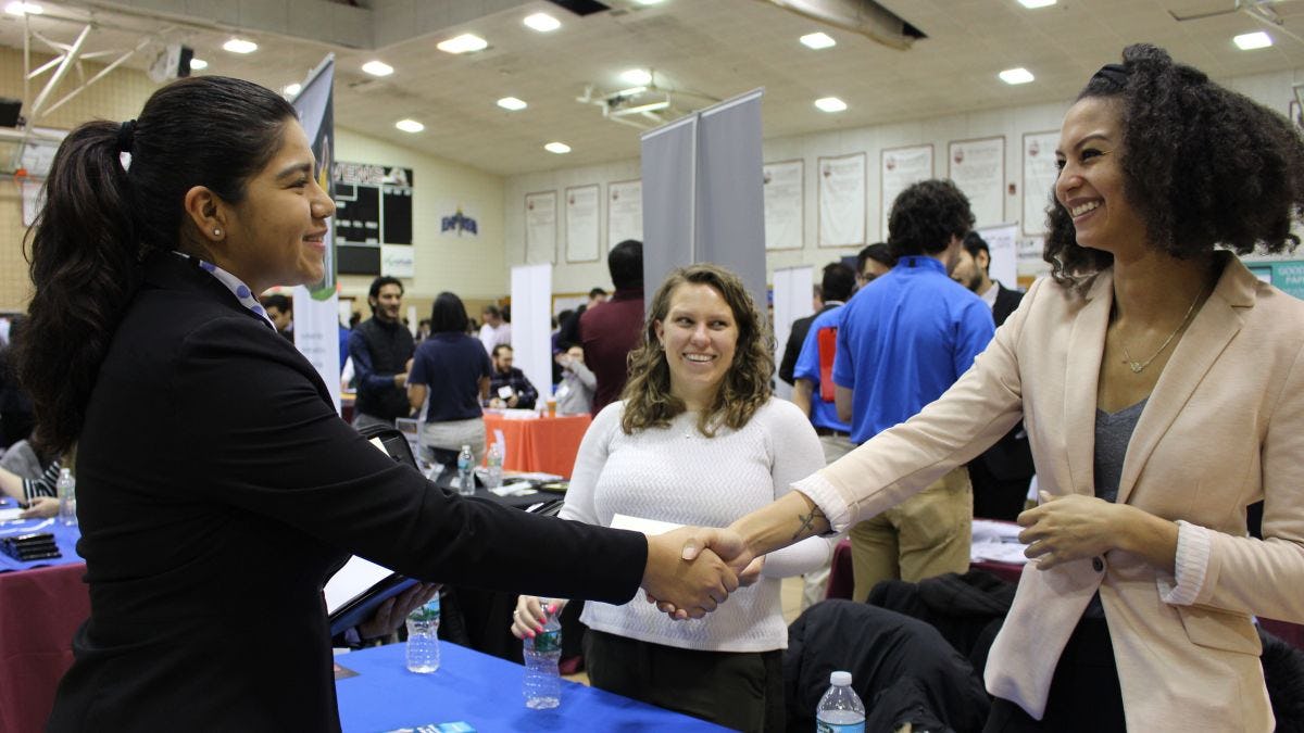 Female student on the left shakes hands with a female recruiter on the right