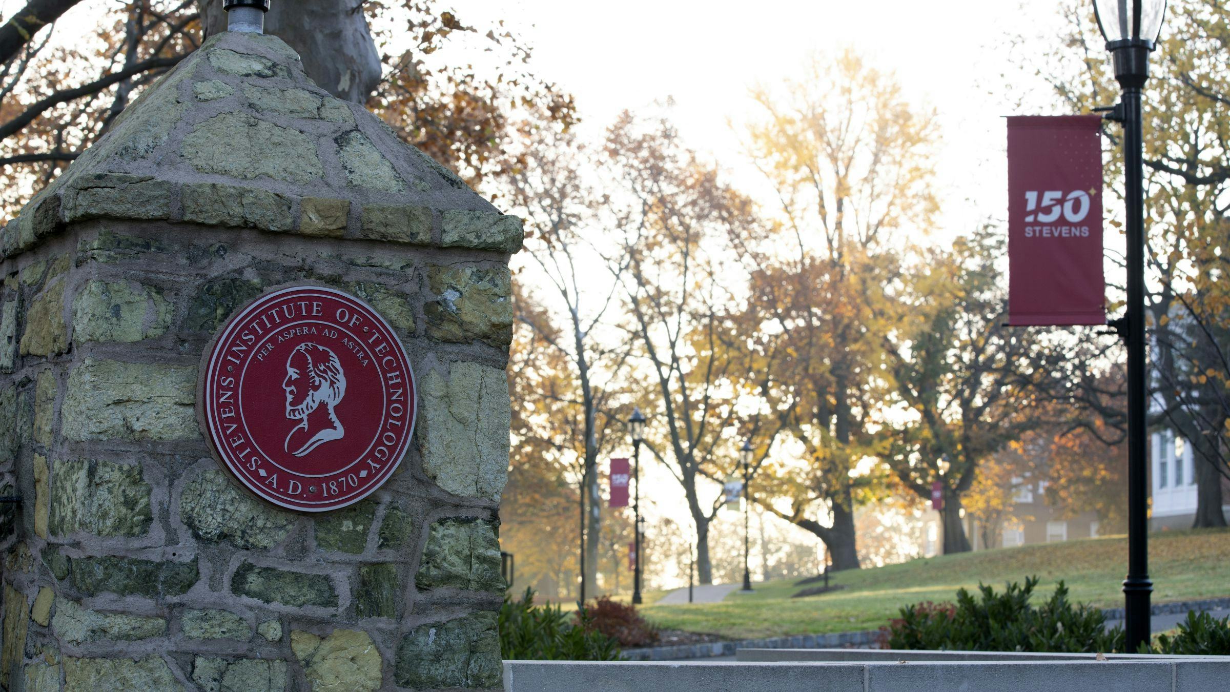 Stevens shield on gateway with trees on campus