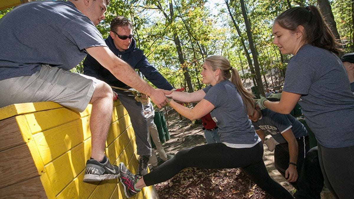 A female student is helped onto an obstacle in the forest course at West Point.
