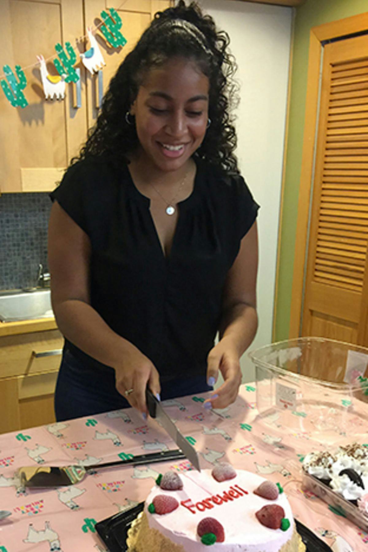 Andrea Gamboa cutting into a farewell cake at the end of her internship.;