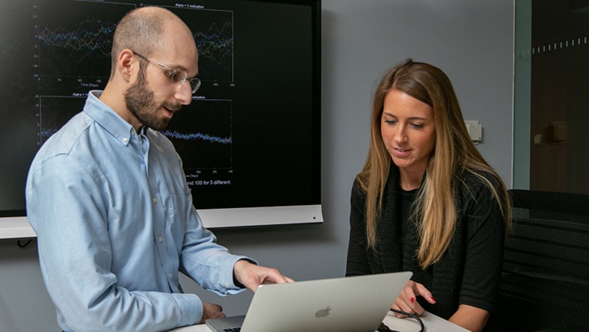 A male professor and female student look at some data on a laptop screen.
