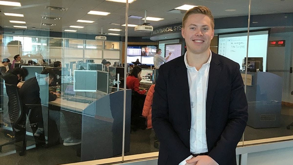Austin McDonnell in a blue blazer standing in front of the high-tech Hanlon Lab, with its rows of Bloomberg terminals.