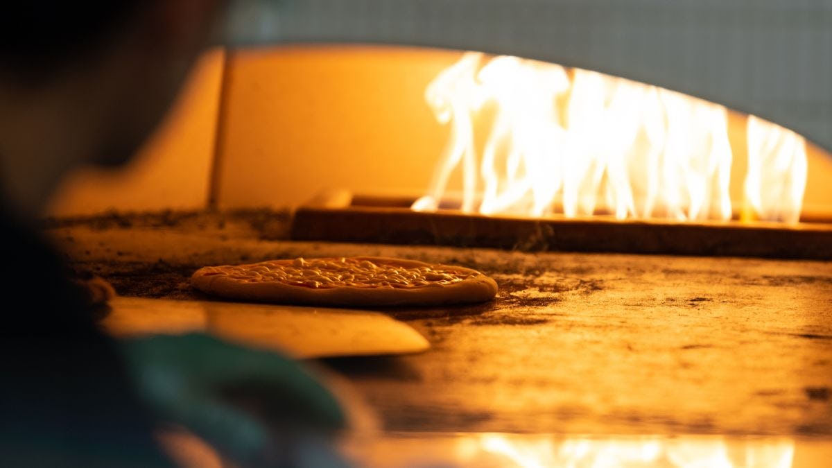 Chef places pizza in flaming hot oven.